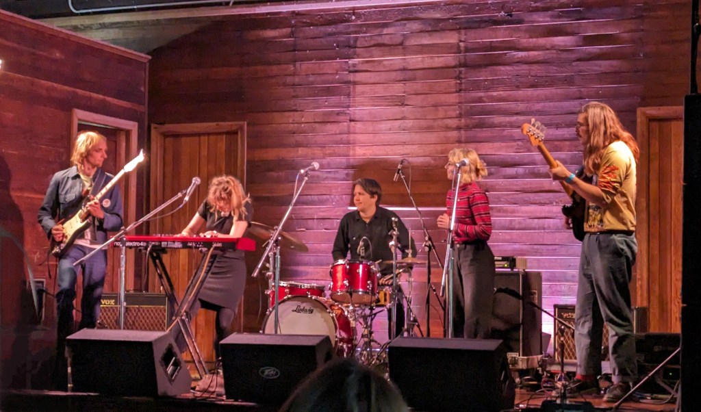 Leah fully absorbed playing keyboard on stage while the rest of the band look to her cues.